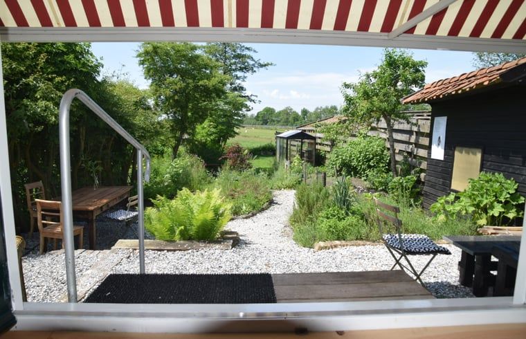 Uitzicht op de groene tuin vanuit Vakantiehuisje in Munnekeburen, Friesland met zonnige veranda.