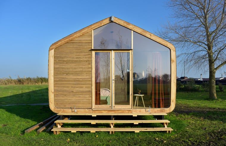 Ferienhaus in Broek in der friesischen Landschaft, modernes Holzhaus mit grosser Glasfassade und Aussicht auf die gruene Umgebung.