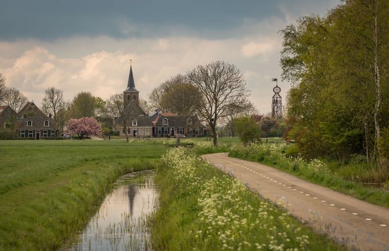 Rustieke omgeving van Huisje in Bears, vakantiehuis op het Friese platteland, met weelderige natuur en serene waterloop in Friesland.
