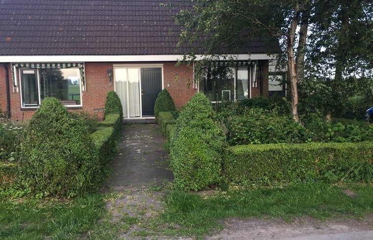 Aussenbereich des Ferienhauses in Nes, Friesland, umgeben von gruenen Hecken.