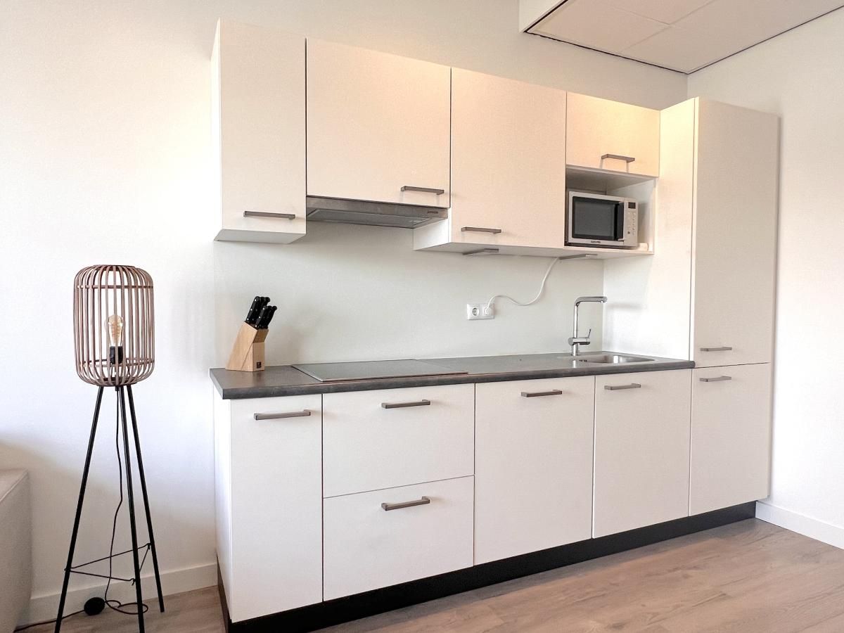 Moderne Kueche im Ferienhaus Havenzicht, Maasbommel, mit schlichten weissen Schraenken und Geraeten in Rivierengebied, Gelderland.