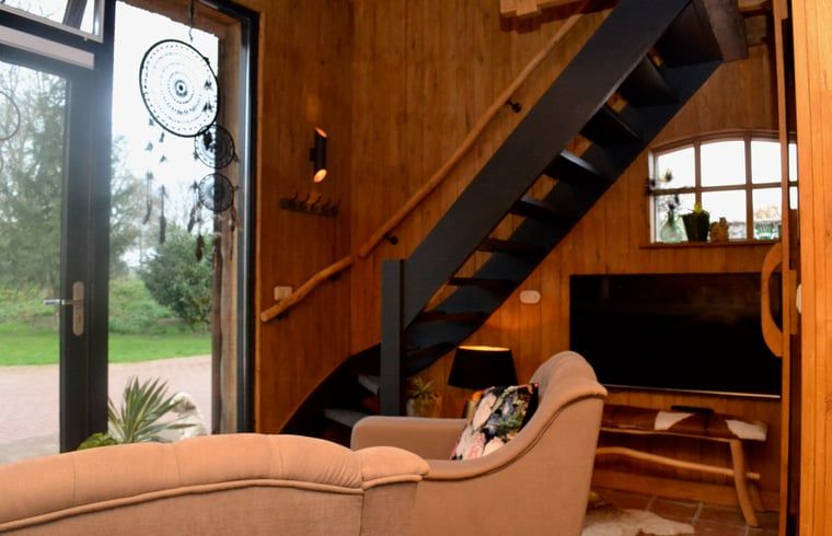 Gezellige binnenruimte van Vakantiehuisje in Ruurlo, Achterhoek, met houten interieur en trap naar bovenverdieping, ideaal voor ontspanning.