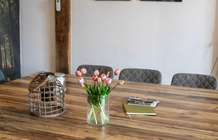 Detail van de eetkamertafel in Huisje in Aalten, vakantiehuis in de Achterhoek, met bloemen en tijdschriften.