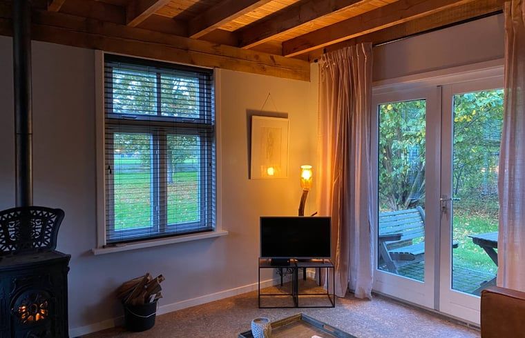 Gemuetliches Wohnzimmer des Ferienhauses in Laren, Achterhoek, Gelderland mit Blick auf den Garten und warmen Holzakzenten.