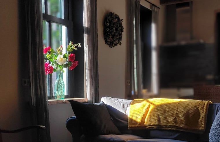 Sonniges Wohnzimmer mit Blumen und Sofa im Ferienhaus in Vragender, Achterhoek, Gelderland.