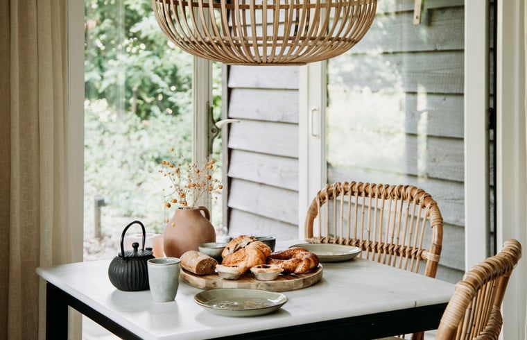 Ontbijttafel in vakantiehuis in Lochem met uitzicht op de groene tuin.