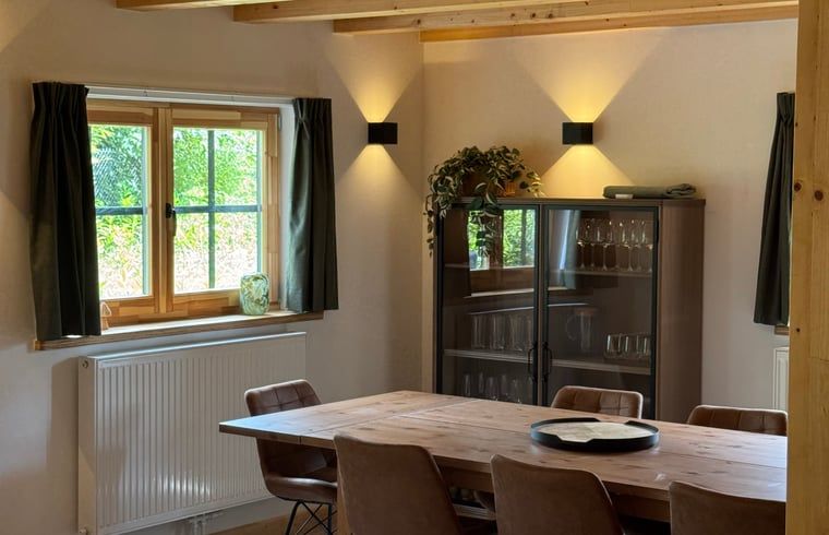 Gezellige eetkamer in Vakantiehuis in Lochem, Achterhoek, met houten tafel en uitzicht op groene tuin, ideaal voor ontspannen verblijf in Gelderland.