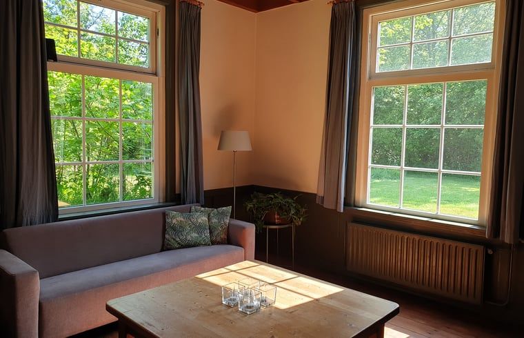 Cozy living room of Holiday Home in Vorden, Achterhoek, with large windows and views of the green nature of Gelderland.