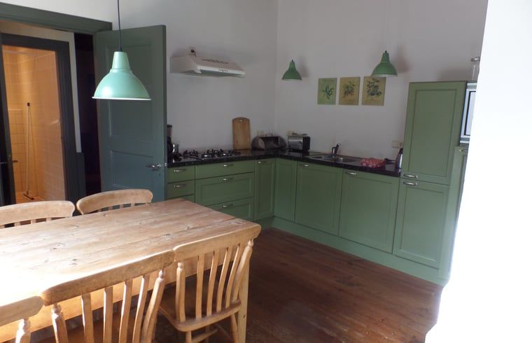 Cozy kitchen in Cottage in Vorden, Achterhoek, Gelderland with wooden dining table and green cabinets for a homely stay.