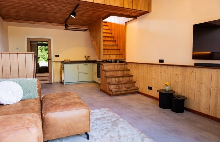 Gezellige woonkamer in Vakantiehuisje in Neede, Achterhoek, met moderne keuken en houten trap.