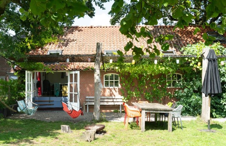 Geniessen Sie den gruenen Garten des Ferienhauses in Lievelde, Achterhoek, Gelderland. Entspannen Sie sich auf der Terrasse mit Haengematten und Sitzgelegenheiten.