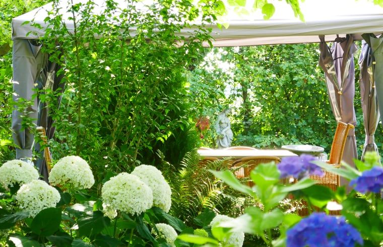 Shaded sitting area in the garden of Cottage in Warnsveld, Achterhoek, surrounded by flowers.