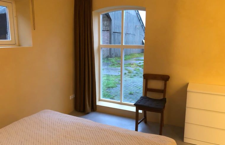 Cottage in Almen, Ferienhaus in Achterhoek, Gelderland. Schlafzimmer mit Gartenblick und bequemem Stuhl.