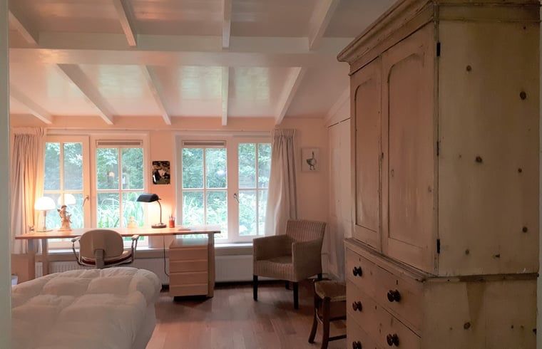 Gemuetliches Schlafzimmer im Ferienhaus in Joppe, Achterhoek, mit Holzmoebeln und Blick auf die gruene Natur durch grosse Fenster.