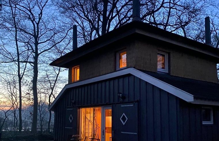 Huisje in Empe, vakantiehuis Gelderland, verlicht bij zonsondergang, omringd door bomen.