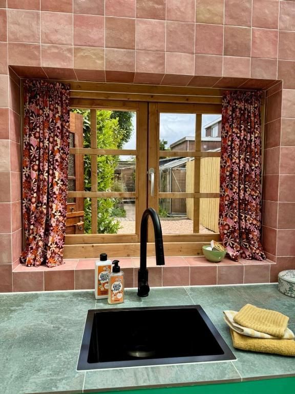 Kuechenfenster mit Aussicht in In de Aap - Apartments & Guesthouse, Bergen, Nordholland, mit bunten Vorhaengen und laendlichem Ambiente.