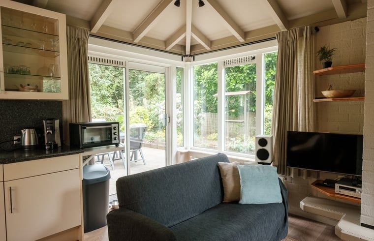Cozy living room of a cottage in Ermelo, Veluwe, Gelderland, with a view of the green garden and modern amenities.