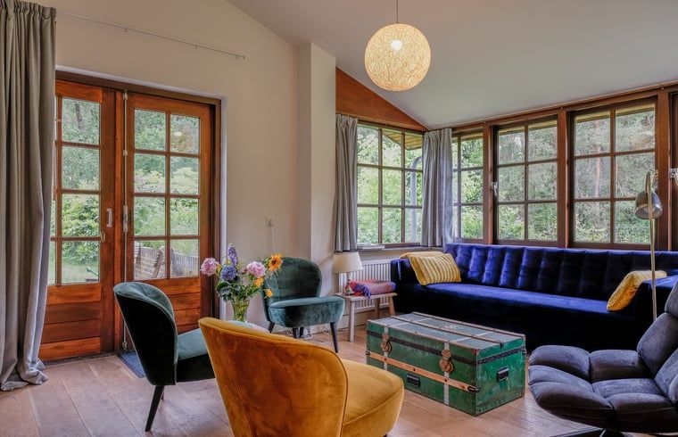 Gezellige woonkamer van Huisje in Ermelo, vakantiehuis op de Veluwe, Gelderland, met uitzicht op de groene natuur door grote ramen.