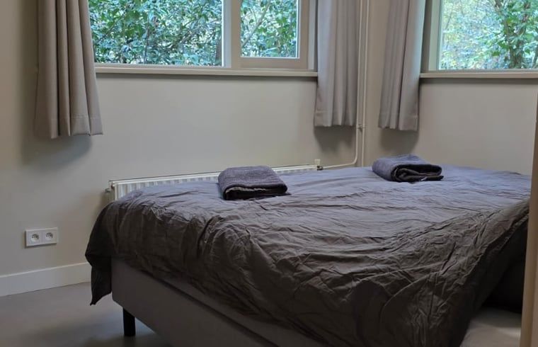 Sfeervolle slaapkamer in Vakantiehuis in Hoenderloo, Veluwe, met comfortabel bed en uitzicht op de groene natuur van Gelderland.