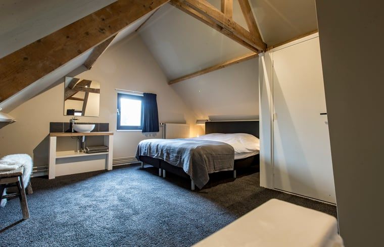 Zolderkamer met houten balken in Huisje in Hoenderloo, Veluwe, voor een rustieke charme.