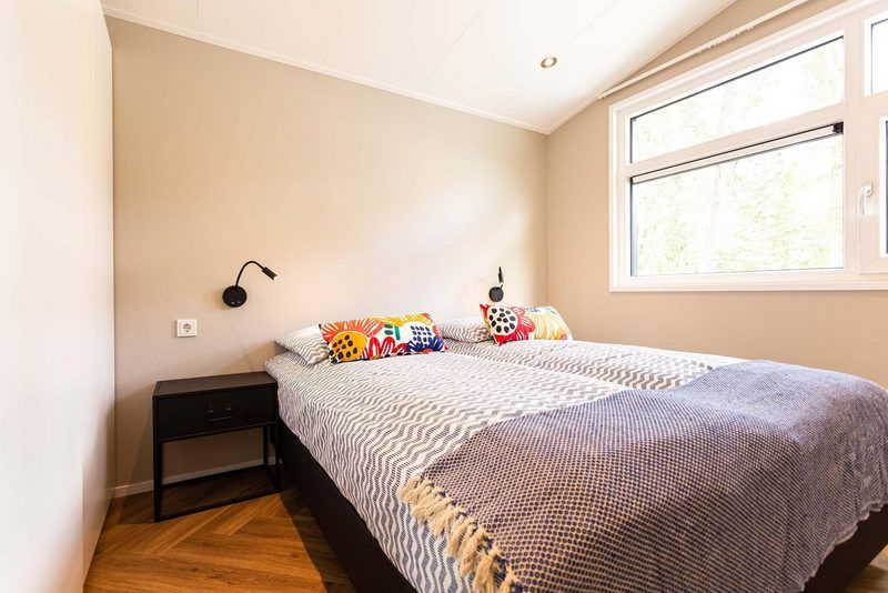 Gemuetliches Schlafzimmer im Silva 5 Personen Sauna Ferienhaus, Garderen, Veluwe mit grossem Fenster und bunten Kissen.