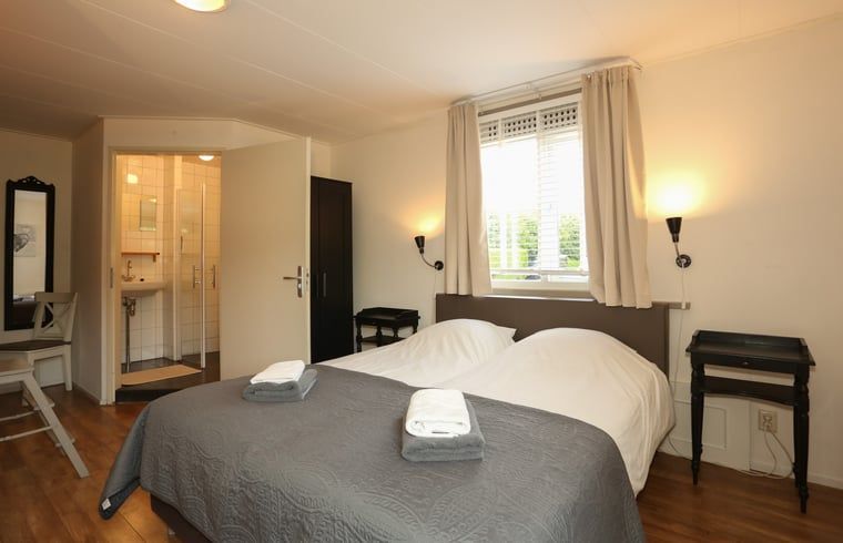 Slaapkamer met tweepersoonsbed en eigen badkamer in Vakantiehuis in Voorthuizen Veluwe.