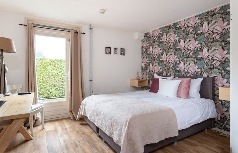 Slaapkamer met bloemenbehang en openslaande deuren in Vakantiehuis in Voorthuizen Veluwe.
