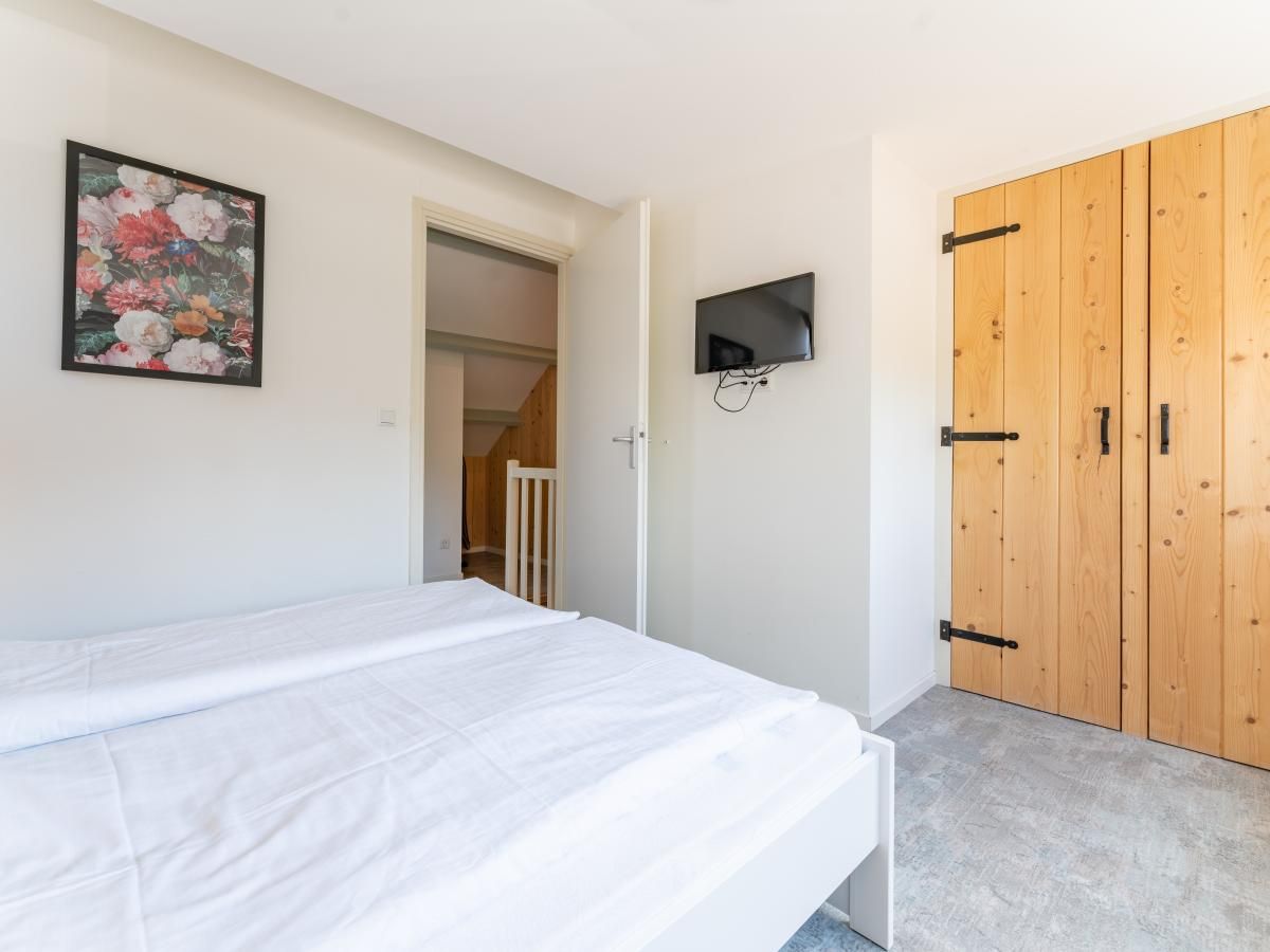 Schlafzimmer im Ferienhaus Pimpelmees in Hulshorst, Veluwe mit TV und Holzschrank.