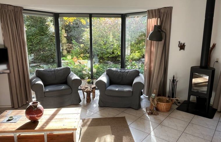 Gezellige woonkamer van Huisje in Epe, Veluwe, met comfortabele stoelen en uitzicht op de groene tuin, ideaal voor ontspanning.