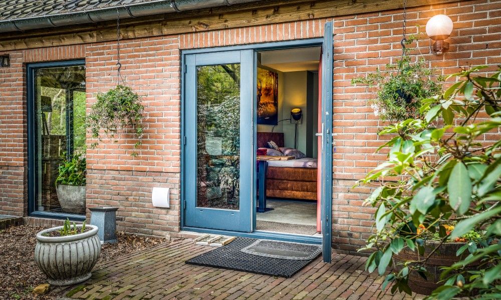 Charmanter Eingang zum Studio REE, Bed and Breakfast in Wekerom, Veluwe mit Gruenpflanzen und Backsteinmauer.