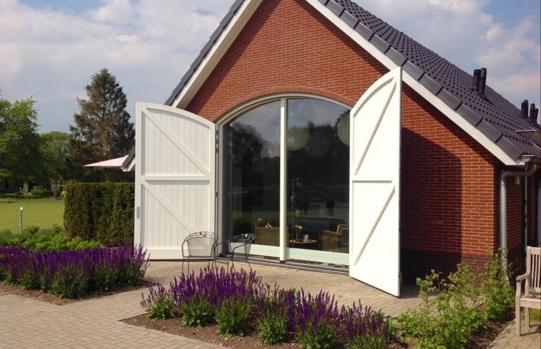 Vakantiehuisje in Eerbeek, Veluwe, Gelderland met prachtige tuin en open deuren, ideaal voor een ontspannen verblijf in de natuur.