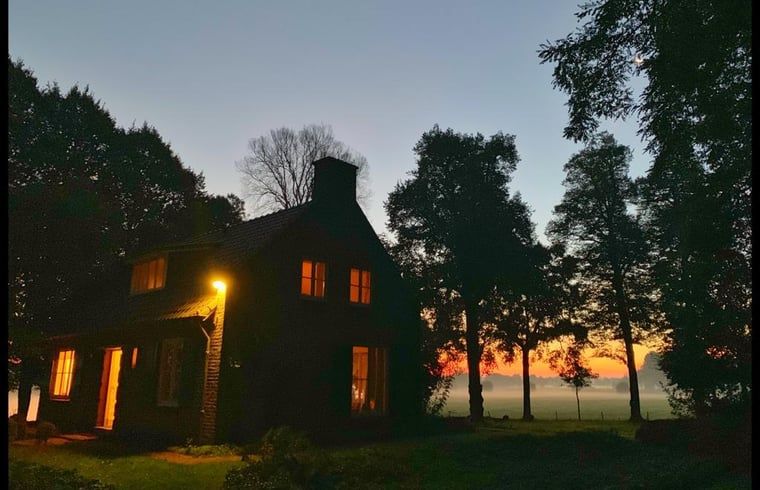 Stimmungsvoll beleuchtetes Landhaus in Geijsteren, Nord-Limburg, umgeben von Baeumen bei Sonnenuntergang.