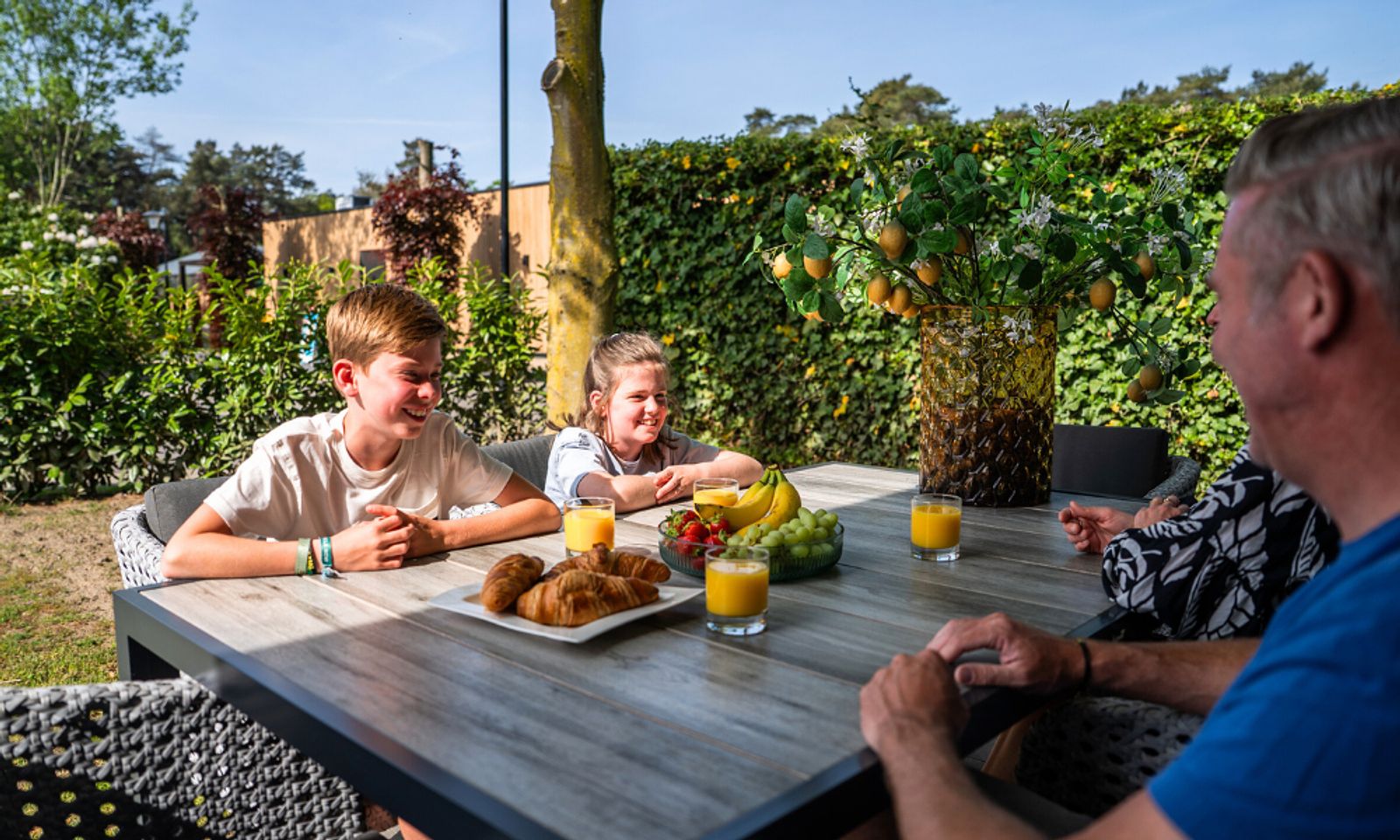Gezin geniet van ontbijt op het terras van White Lodge vakantiehuis, Veldhoven, Kempen, Noord Brabant.