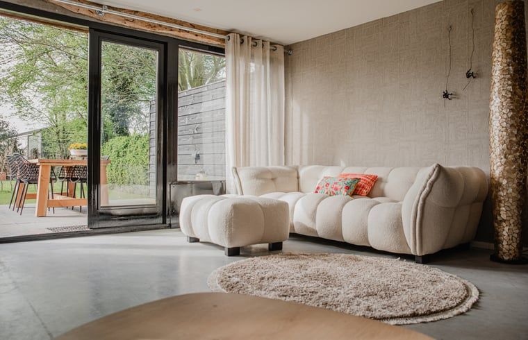 Gemuetliches Wohnzimmer im Ferienhaus in Leende, Nordbrabant mit bequemem Sofa und Gartenblick. Perfekt zum Entspannen.