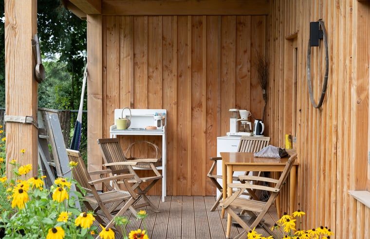 Veranda van Huisje in Best, vakantiehuis in Best, Hart van Brabant, Noord Brabant, met houten zitmeubelen en bloemen.