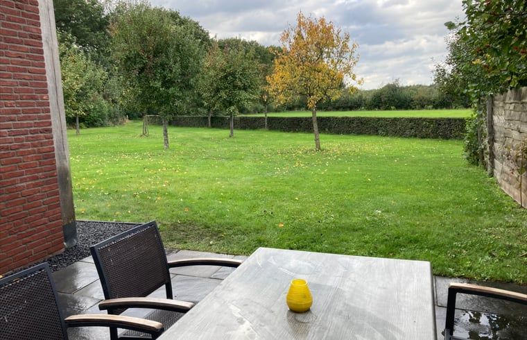 Buitenterras met uitzicht op groene tuin in Vakantiehuis in Schaijk, Noordoost Brabant, ideaal voor buitenmaaltijden.