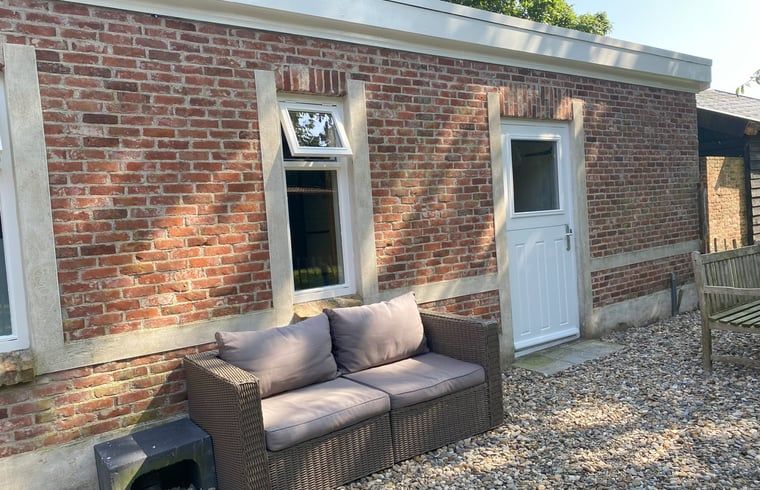 Hinterhof von Cottage in Hoogerheide, Ferienhaus in Nordbrabant mit einer gemuetlichen Aussenbank und gruener Umgebung.