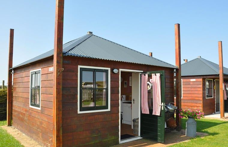 Gemuetliches Ferienhaus in Julianadorp an der Nordseekueste, Nordholland, mit rustikaler Holzfassade und einladender offener Tuer.