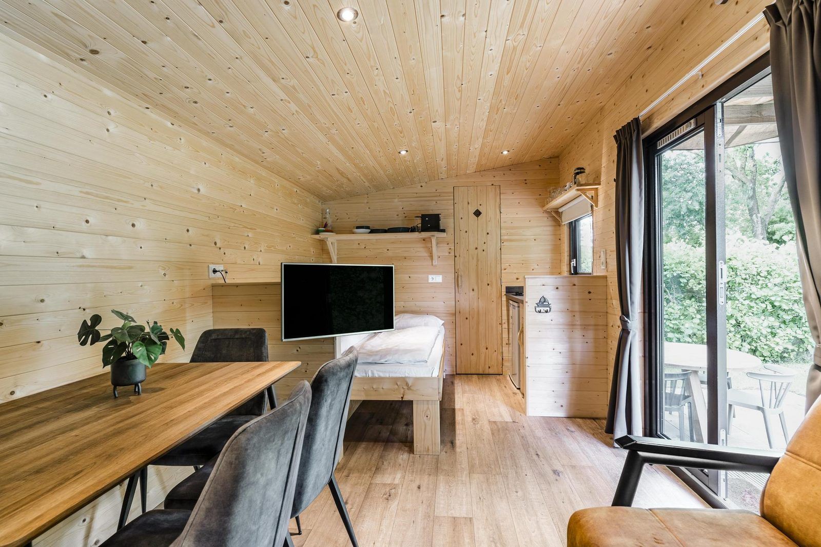 Gemuetliches Zimmer in der Woodlodge fuer 4 Personen in Julianadorp, Nordseekueste, Nordholland mit Holzausstattung und Blick auf die Terrasse.