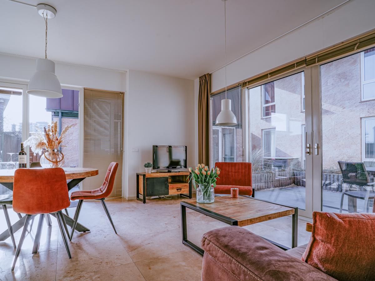 Gemuetliches Wohnzimmer des Ferienhauses Zeebaars in Egmond aan Zee, Nordholland, mit Blick auf die Terrasse an der Nordseekueste.