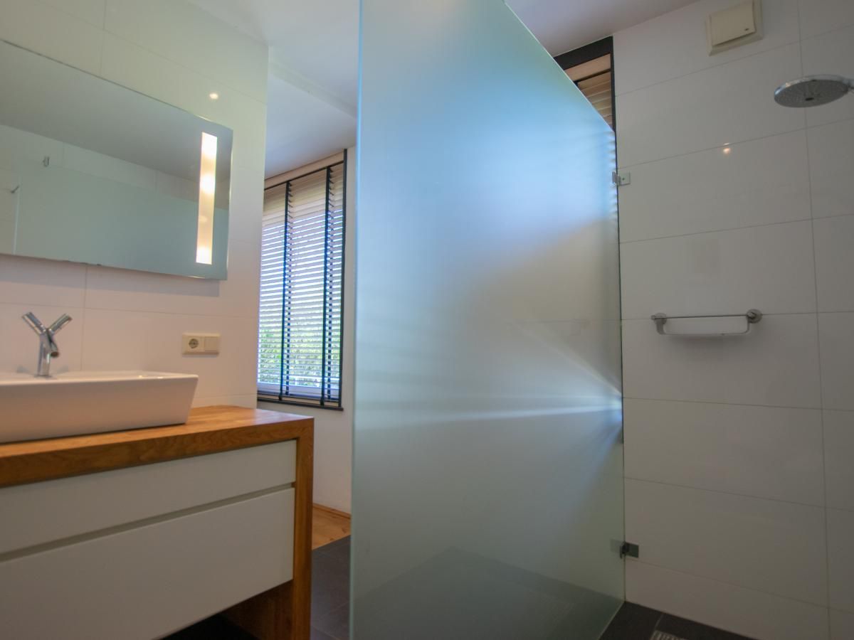 Moderne badkamer in Landhuis Duinzicht, vakantiehuis in Callantsoog aan de Noordzeekust, Noord-Holland, met ruime inloopdouche en elegant wastafelmeubel.