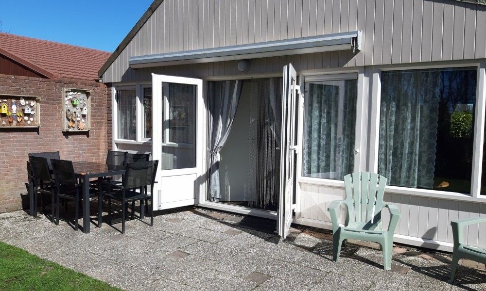 Veranda van vakantiehuis Rekere 111 in Schoorldam, Noordzeekust, Noord-Holland met zitgelegenheid en open deuren.