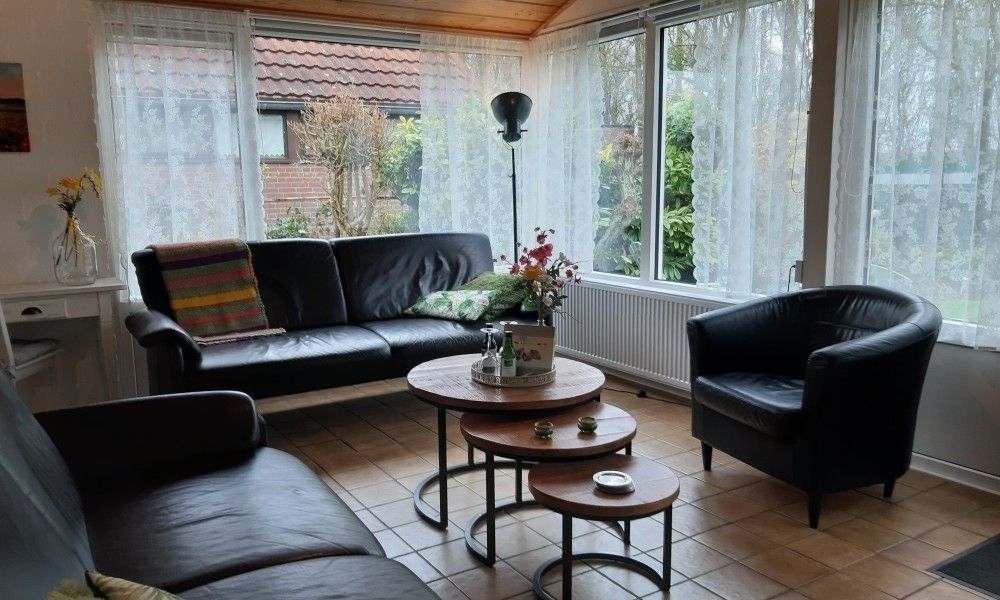 Lichte zithoek in vakantiehuis Rekere 111, Schoorldam, Noordzeekust, Noord-Holland met grote ramen en comfortabele stoelen.
