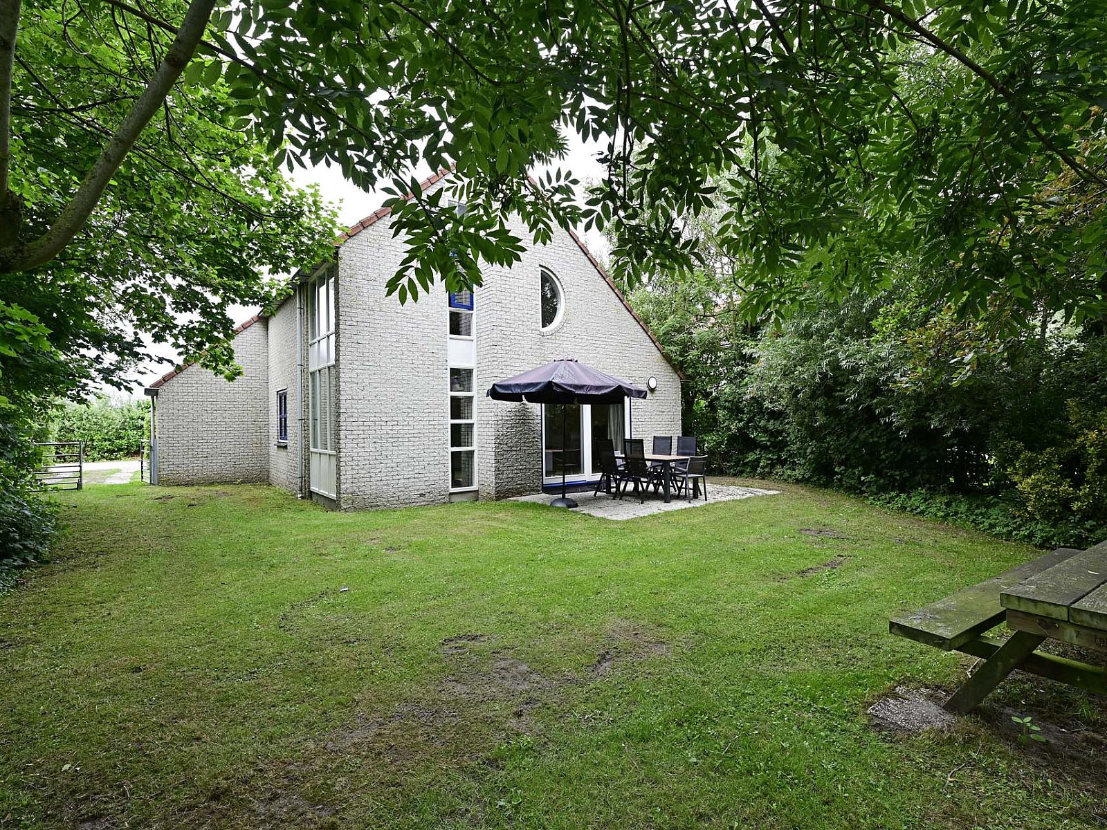 Terras van vakantiehuis in Julianadorp aan Zee met tuinmeubilair en parasol.