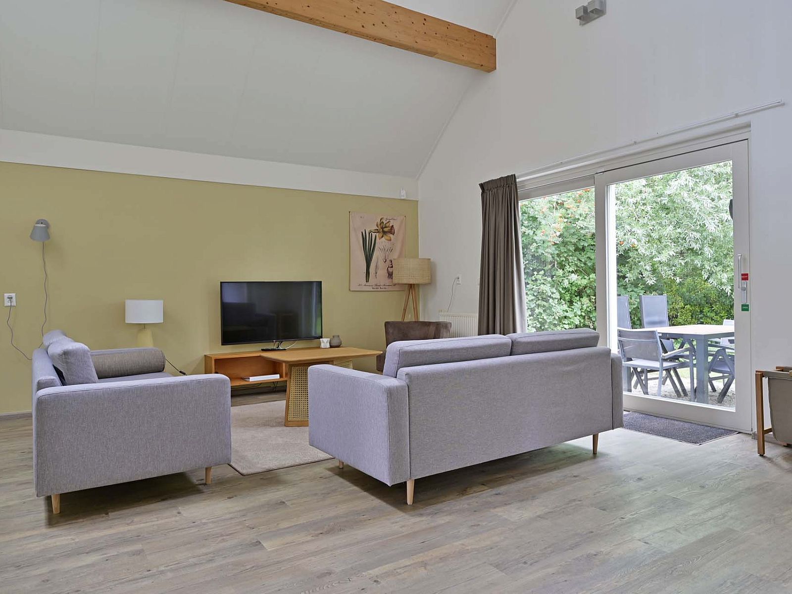 Woonkamer met schuifpui naar tuin in vakantiewoning Julianadorp aan Zee, Noord-Holland.