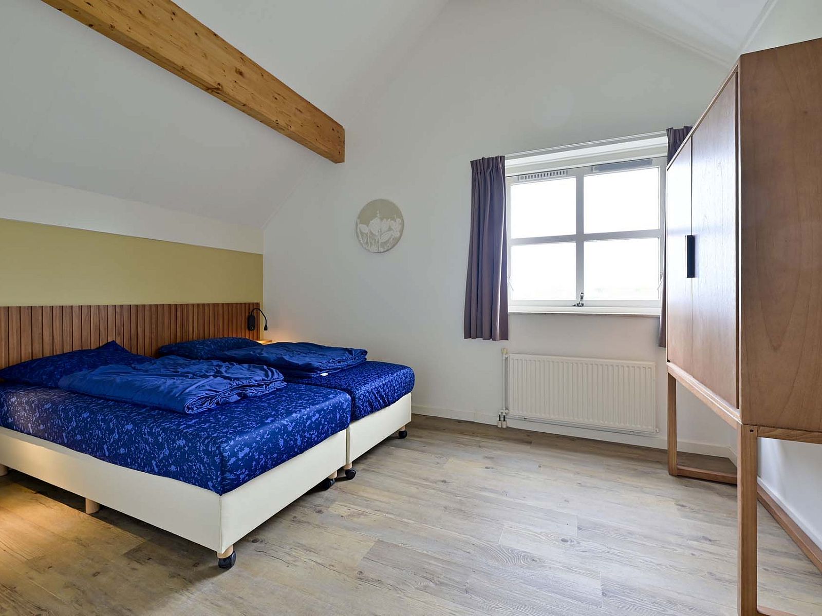 Slaapkamer met houten balken en tweepersoonsbed in Julianadorp aan Zee.