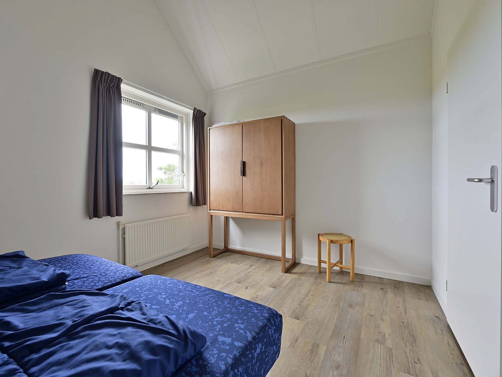 Ruime slaapkamer met houten vloer in vakantiewoning Julianadorp aan Zee.