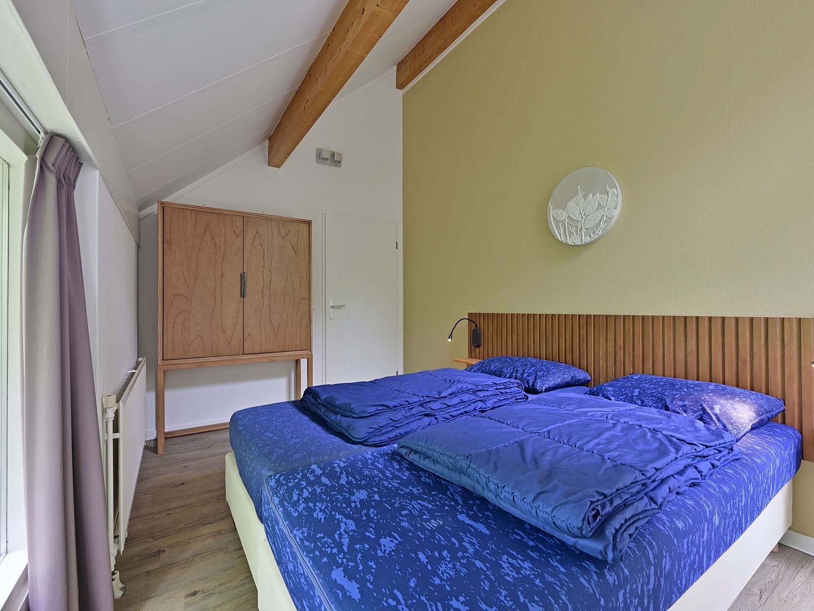 Slaapkamer met houten details en uitzicht op natuur in vakantiewoning Julianadorp aan Zee.