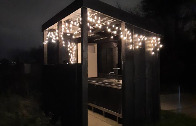 Sfeervolle buitenkeuken bij nacht in Huisje in Zuid-Scharwoude, een vakantiehuis in Noord-Holland, met gezellige verlichting.