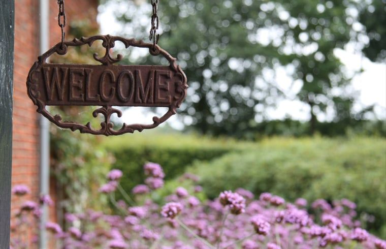 Willkommensschild am Eingang des Ferienhauses in Mander, Twente, Overijssel, umgeben von schoenen Blumen und Gruenanlagen.
